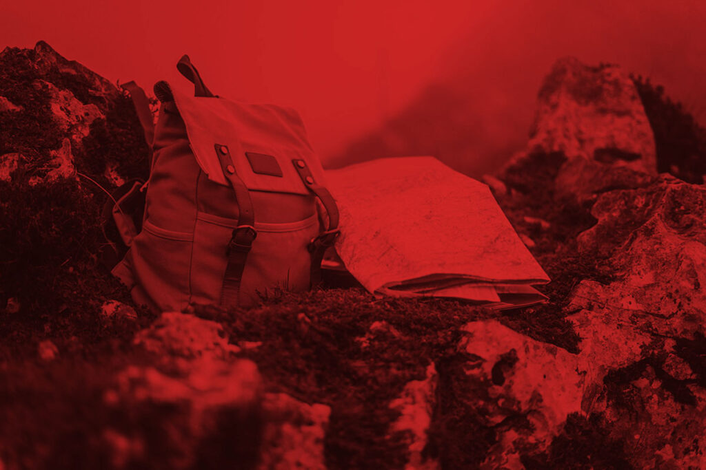 A backpack and map sitting on a rock colorized red.