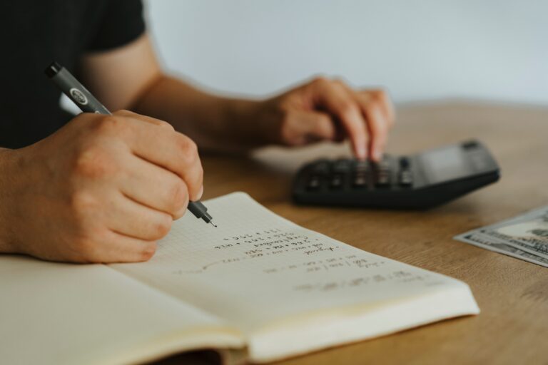 Image of a hand writing and another one on a calculator for the blog, Preparing Your Financials for a Business Transition Starts Years Before the Transaction