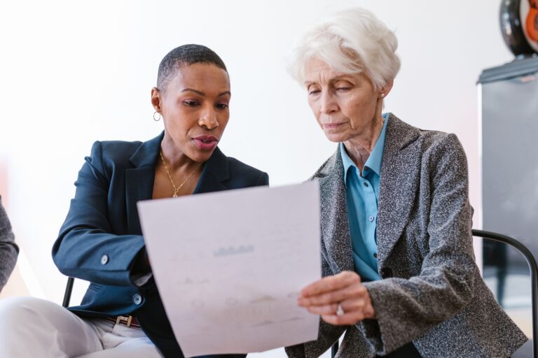 Image of two women discussing a document for the blog, How Two Business Transitions Shaped the Second Edition of It’s a Journey.